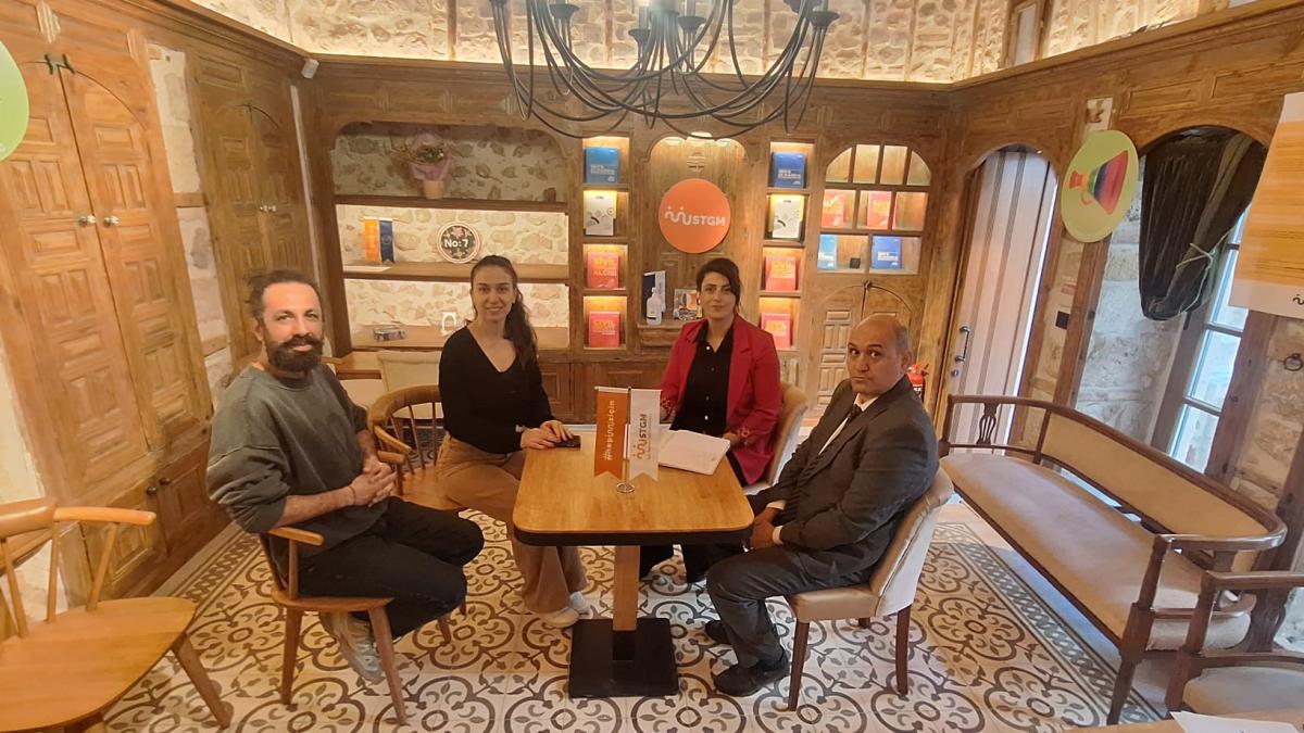 Kafede bir masada oturan dört kişi, arka planda kitaplı raflar.