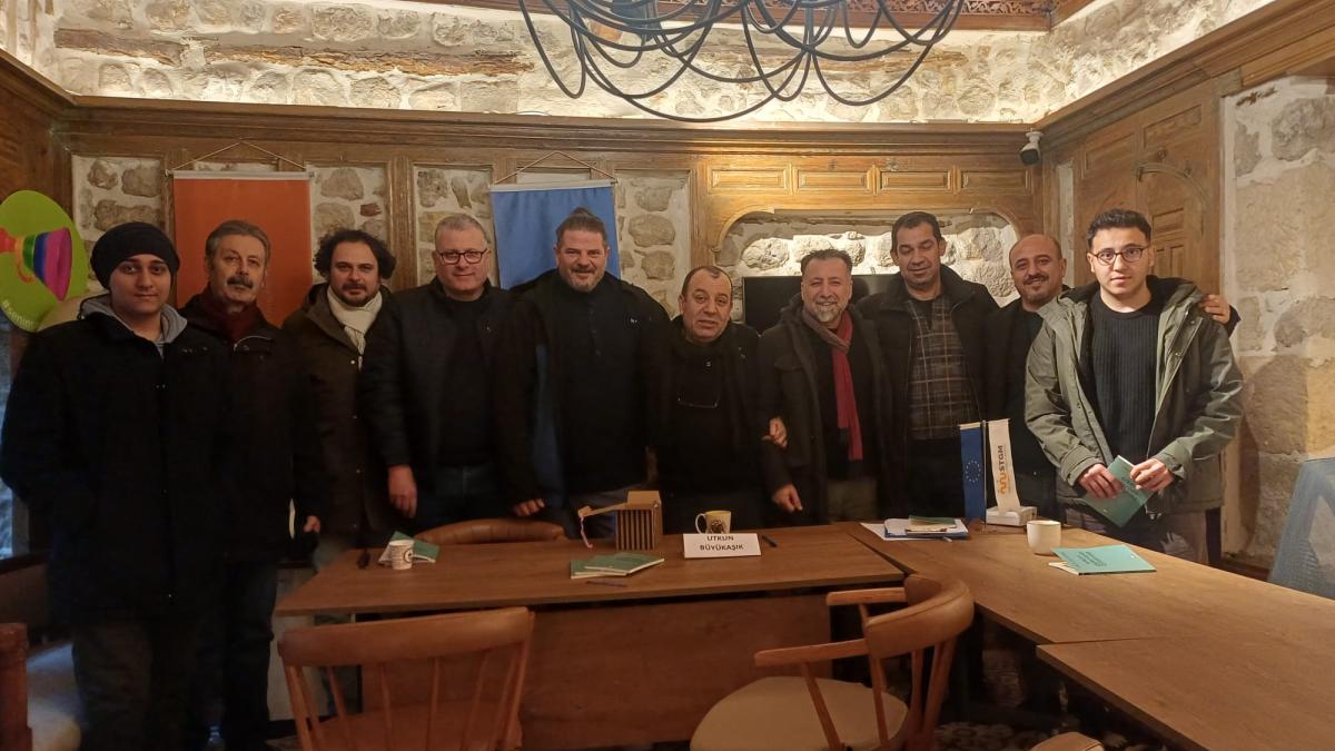 Ahşap bir odada, bir masa arkasında yan yana duran on kişi.