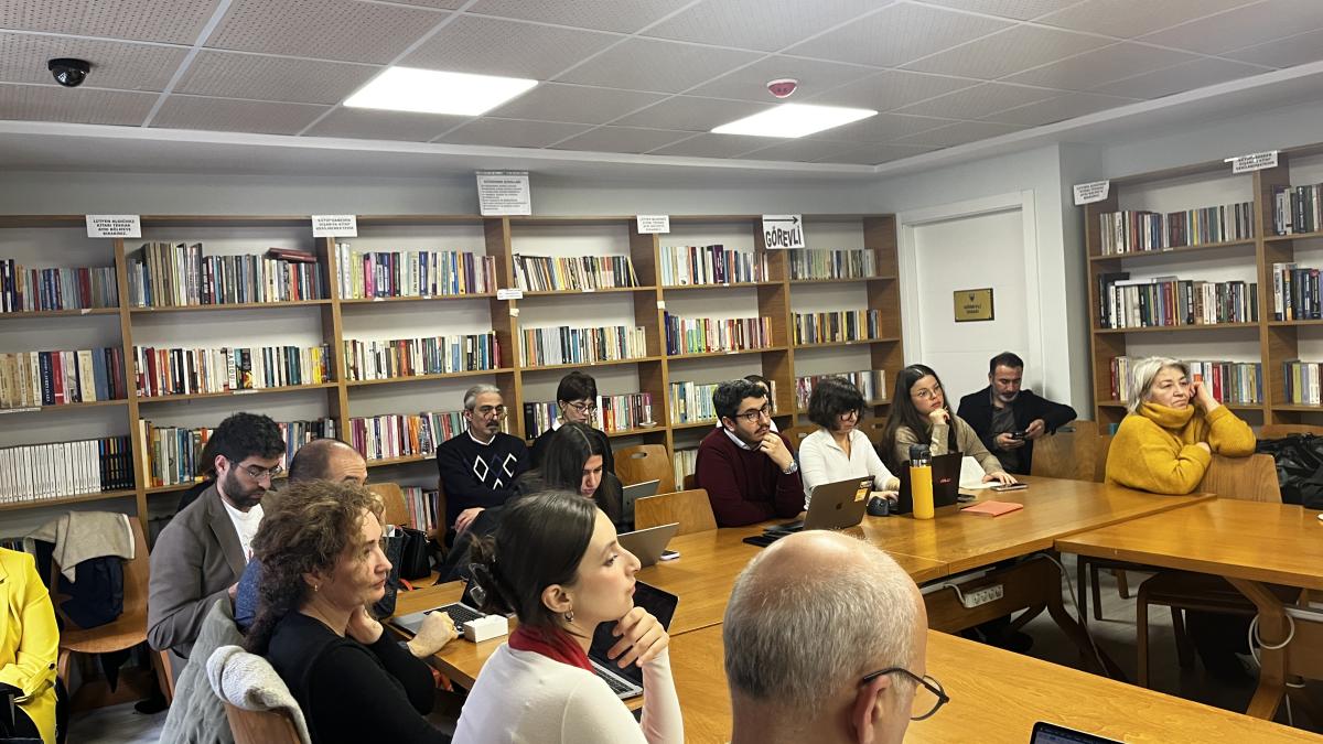 Raflarda kitapların olduğu bir kütüphanede toplantı yapan insanlar.