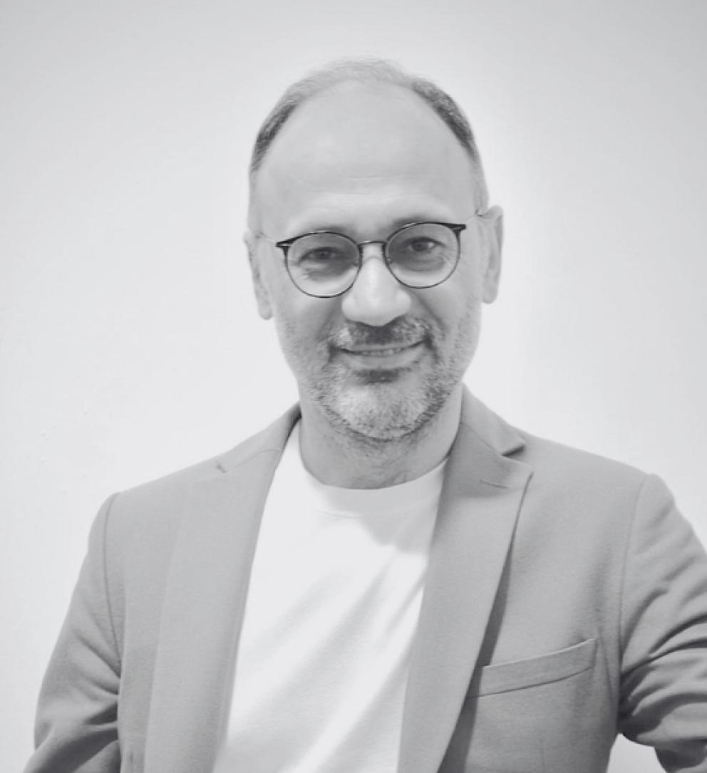 Gözlüklü, sakallı adam takım ceket ve tişörtle gülümsüyor.